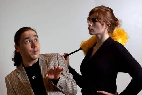 Ein Mann schaut eine Frau von links unten nach oben an, Frau hält Staubwedel in der Hand unZwei Personen, eine mit Sonnenbrille und Staubwedel, die andere überrascht schauend.d blickt desinteressiert