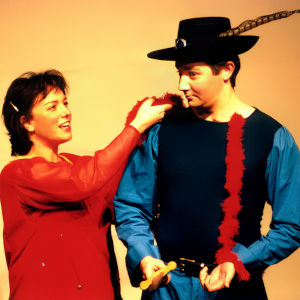 Zwei Personen in Kostümen, eine mit Hut und Feder, die andere mit rotem Schal.